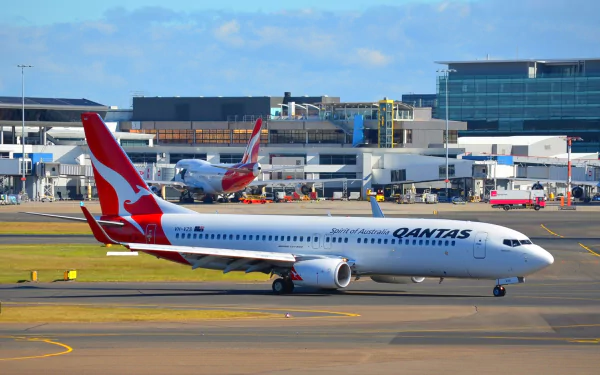 A Qantas Boeing 737 aircraft taxis on the runway, with airport facilities in the background, creating a vibrant HD desktop wallpaper.