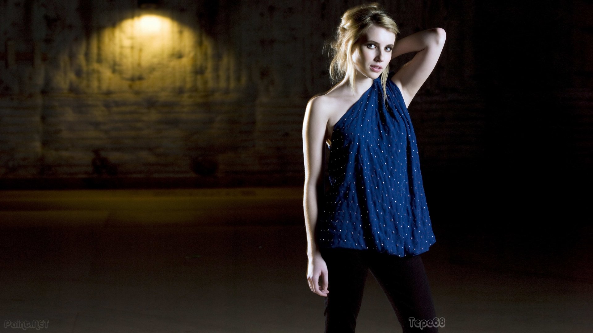 A 4K Ultra HD desktop wallpaper featuring celebrity Emma Roberts in a dark, moody setting, wearing a blue one-shoulder top with a softly lit brick wall background.