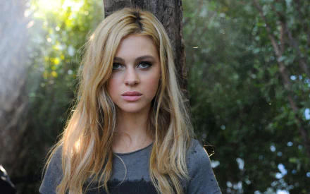 HD PC desktop wallpaper featuring American actress and celebrity Nicola Peltz with long blonde hair, standing outdoors against a blurred natural background.