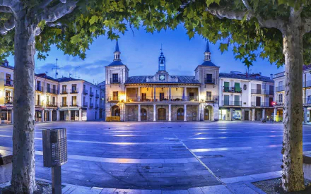 Religious church in a town square at dusk — HD PC desktop wallpaper and background showing illuminated bell towers, arched façade and a tree-framed plaza.
