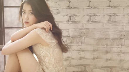 HD PC desktop wallpaper featuring IU in a soft, serene pose against a textured white brick wall, highlighting her music and calming presence.