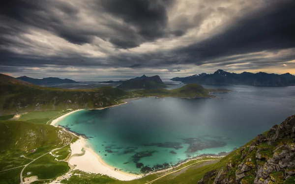 HD desktop wallpaper showcasing Norway’s coastline with turquoise sea, ocean bay, and dramatic mountain landscape under a cloudy sky.