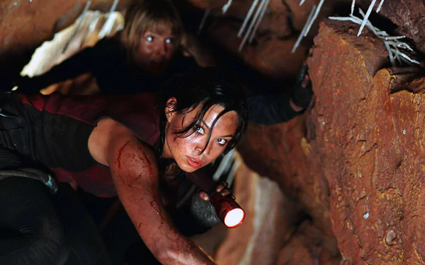HD PC desktop wallpaper from the movie The Descent: blood-smeared woman crawls through a narrow cave with flashlight, stalactites overhead and a claustrophobic, tense horror atmosphere.