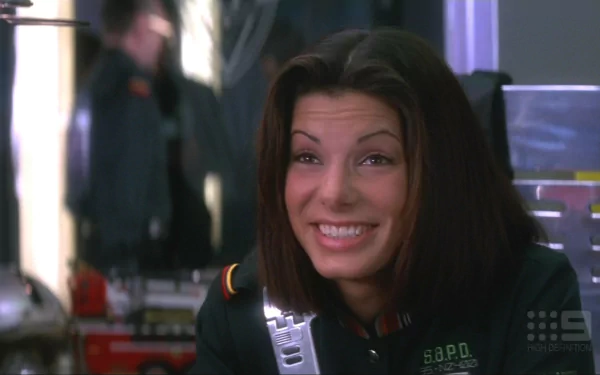 HD PC desktop wallpaper of a smiling woman in a futuristic police uniform from the movie Demolition Man, close-up with a blurred high-tech background.
