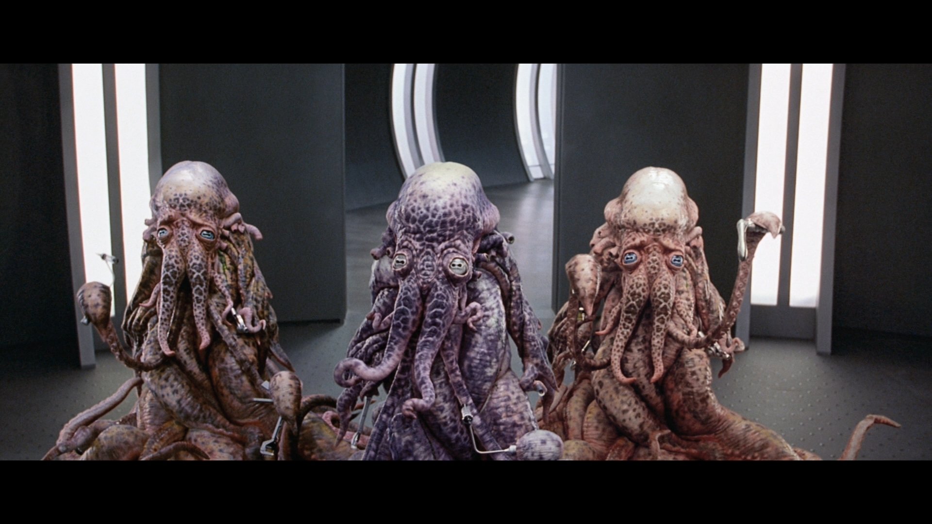 HD PC desktop wallpaper: three tentacled alien beings from the movie Galaxy Quest in a sleek sci‑fi corridor, richly textured and atmospheric.