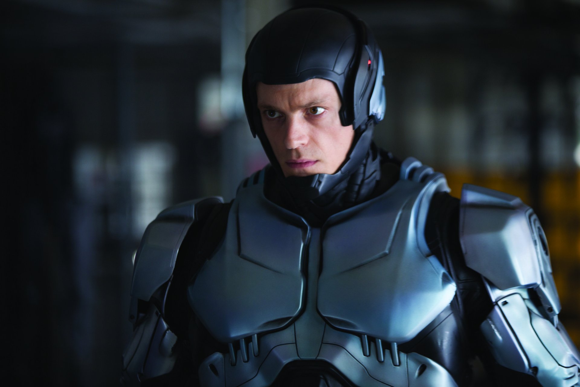 Robocop (2014) movie 2K Quad HD PC desktop wallpaper: close-up of the armored cyborg in a dark metallic suit, helmetless with an intense gaze, blurred industrial background.