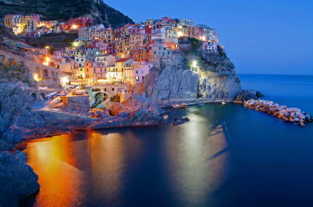 A stunning HD wallpaper of Manarola, Cinque Terre, Italy, showcasing colorful man-made buildings perched on cliffs, reflecting beautifully in the calm evening sea.