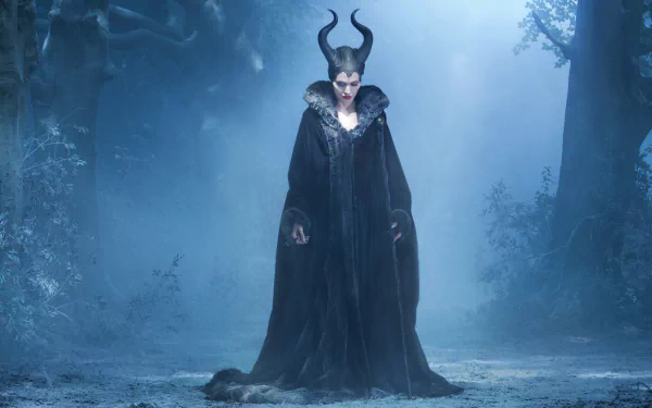 Angelina Jolie as Maleficent stands majestically in a mystical forest, shrouded in an atmospheric blue light, creating a striking 4K Ultra HD desktop wallpaper.