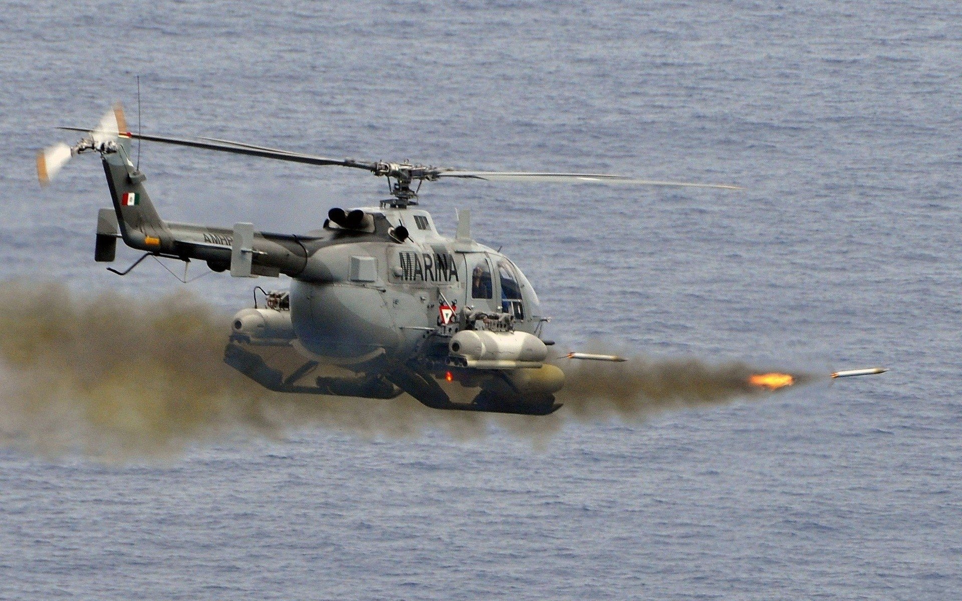 Military MBB Bo 105 in HD PC desktop wallpaper and background: helicopter firing rockets over open ocean at low altitude.