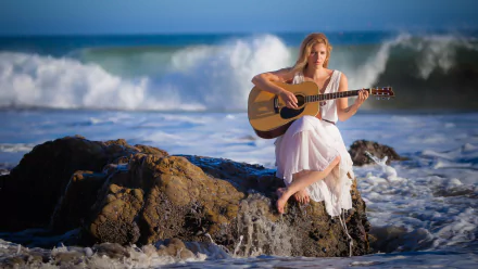 A woman in a white dress playing a guitar while sitting on seaside rocks with waves crashing around her, capturing a serene and introspective mood. HD desktop wallpaper and background.
