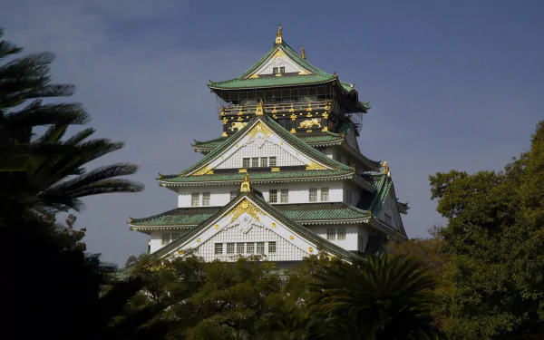 HD desktop wallpaper showcasing Osaka Castle, a historic man-made Japanese landmark framed by lush greenery under a clear blue sky.