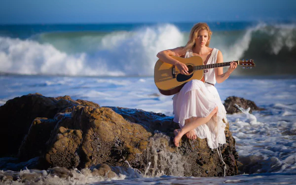 A woman in a white dress playing a guitar while sitting on seaside rocks with waves crashing around her, capturing a serene and introspective mood. HD desktop wallpaper and background.