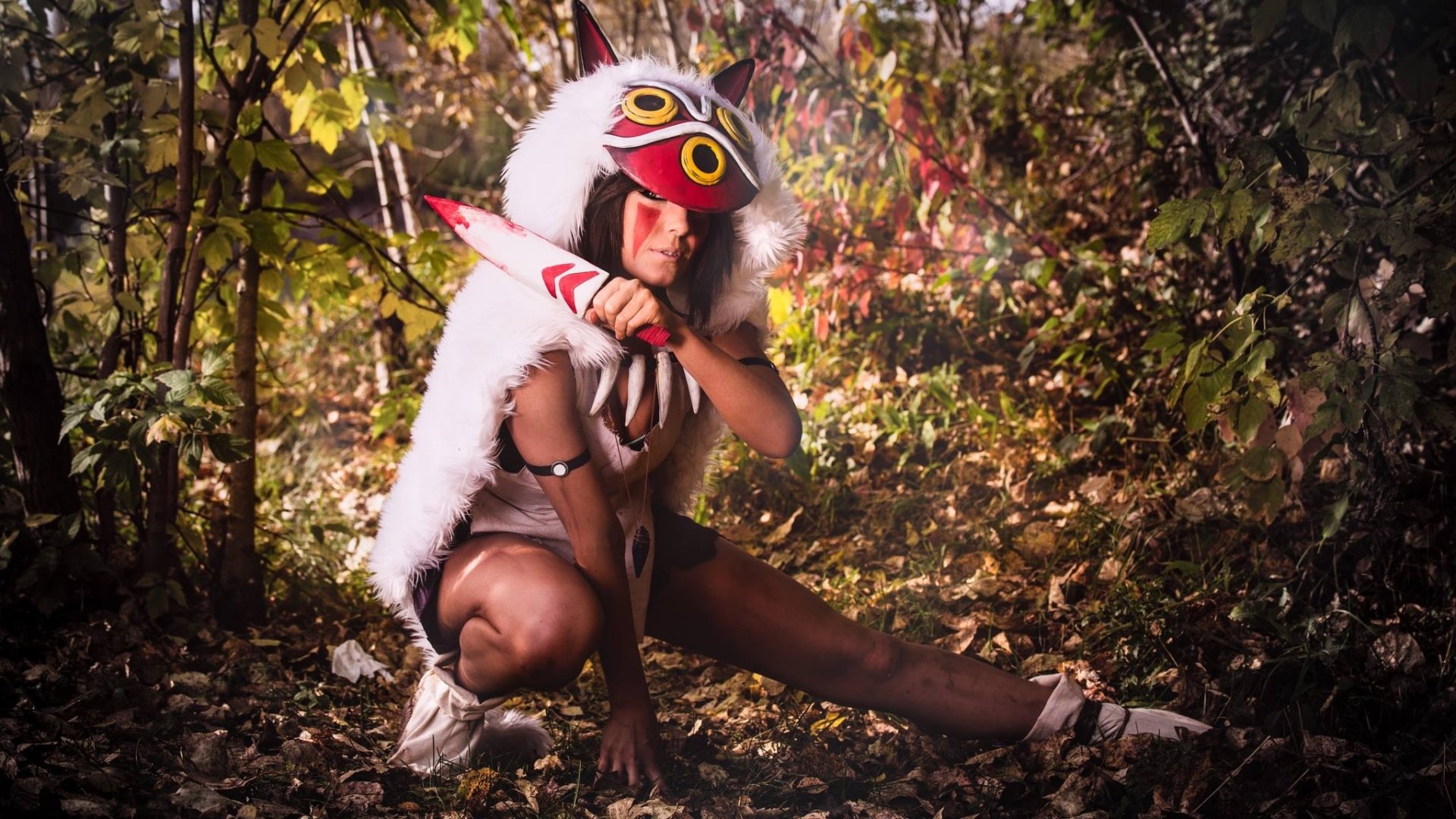 HD PC desktop wallpaper featuring a woman in detailed cosplay crouching in a forest setting, surrounded by autumn foliage.