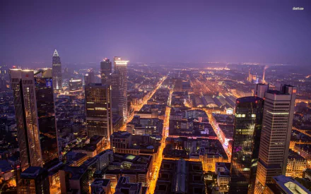 A nighttime aerial view of Frankfurt's illuminated cityscape with high-rise buildings and streets glowing under a deep blue sky, captured as an HD man-made desktop wallpaper.
