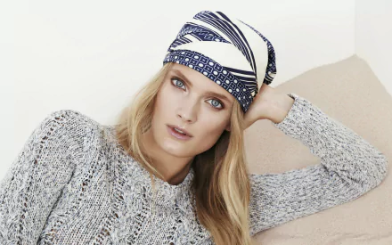 2K Quad HD desktop wallpaper of a blonde woman model reclining on a couch, wearing a knit sweater and patterned headscarf, gazing directly at the camera.