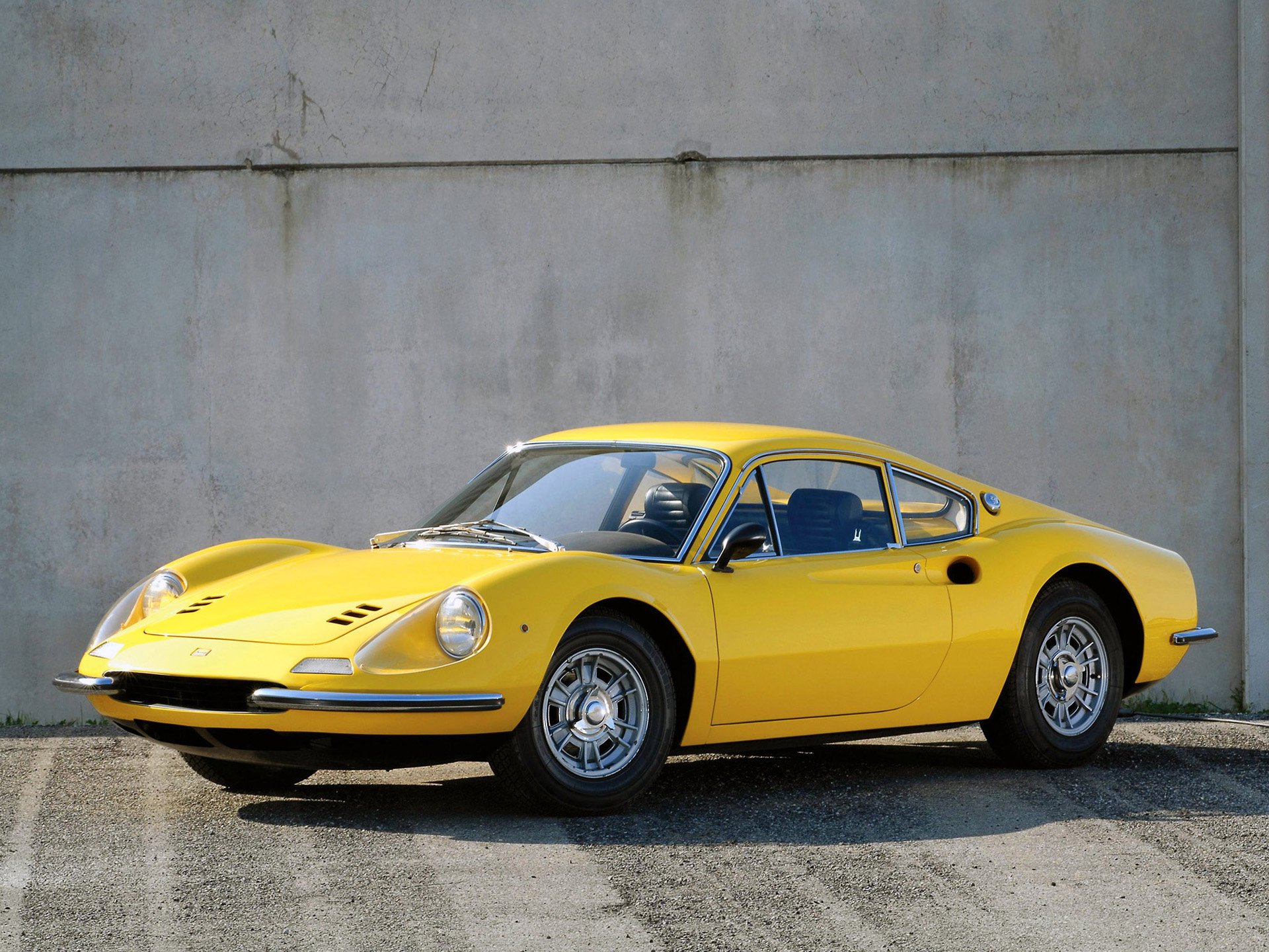Yellow Ferrari Dino 206 GT sports car parked by a concrete wall — classic Ferrari vehicle, HD PC desktop wallpaper and background.