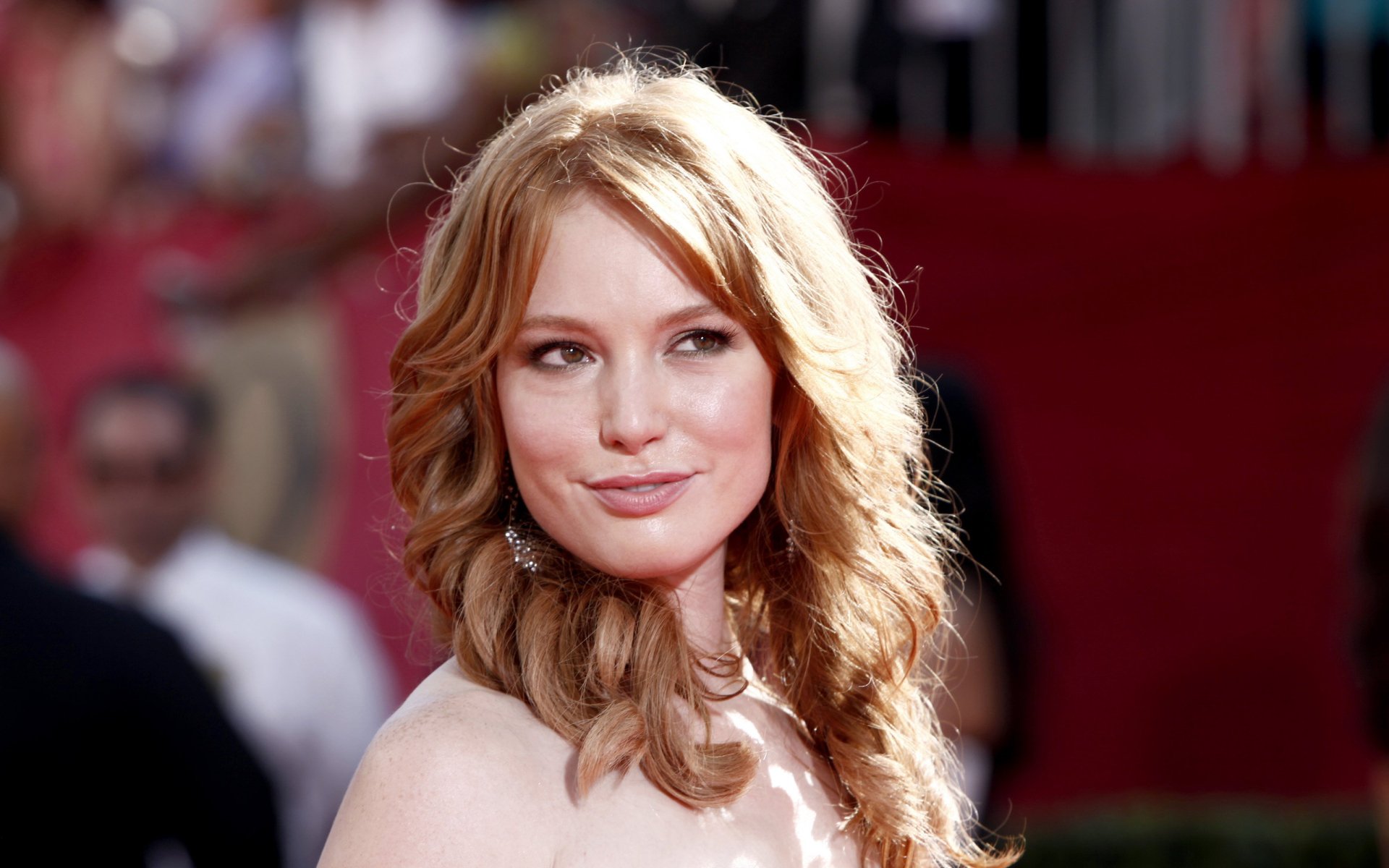 HD desktop wallpaper featuring American actress Alicia Witt with wavy blonde hair, smiling softly against a blurred red carpet background.