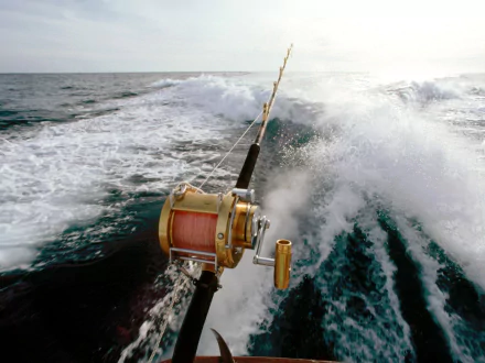 HD PC desktop wallpaper showing a fishing rod with reel casting into turbulent ocean waves, capturing the action and sport of deep-sea fishing.
