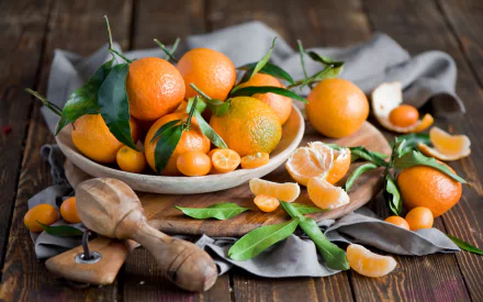 HD desktop wallpaper showing fresh mandarins with green leaves on a wooden table, some whole and some peeled, highlighting vibrant food colors and textures.