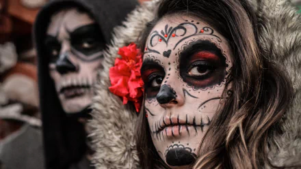 Artistic sugar skull face paint on a woman with a red flower in her hair, captured in stunning 4K Ultra HD for a striking PC desktop wallpaper.