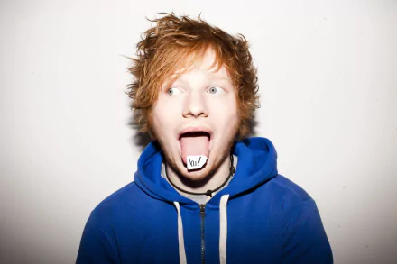 HD desktop wallpaper and background featuring Ed Sheeran. The musician is wearing a blue hoodie and has his tongue out with the word bit on it.