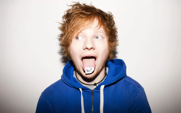 HD desktop wallpaper and background featuring Ed Sheeran. The musician is wearing a blue hoodie and has his tongue out with the word bit on it.