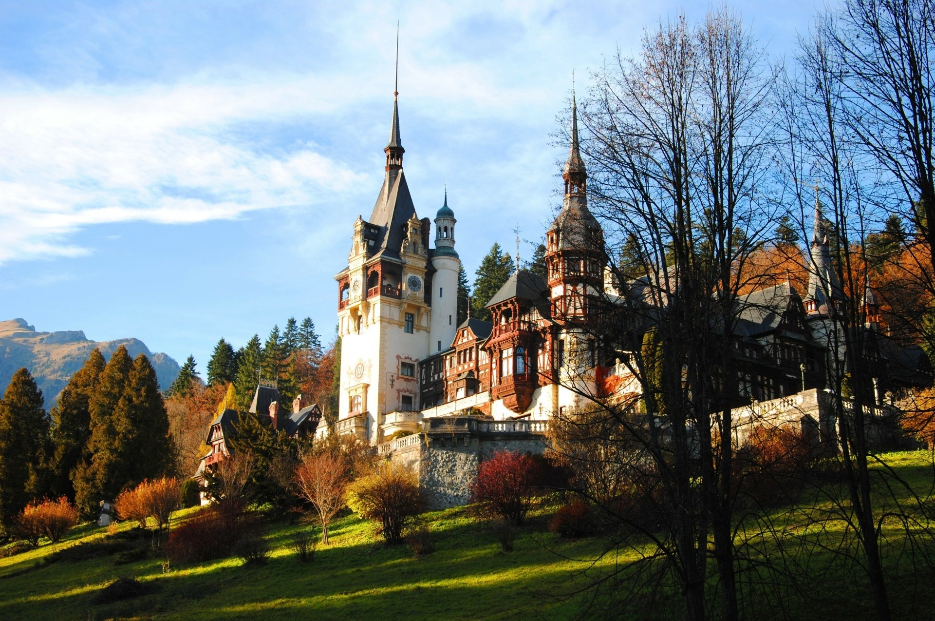 Peleș Castle in Romania showcases stunning architecture amid autumn foliage, with majestic towers rising against a clear blue sky, offering a picturesque scene of man-made beauty.