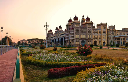 A scenic view of Mysore Palace in India, showcasing its stunning architecture amid vibrant gardens at sunset, offering a breathtaking backdrop for any desktop.