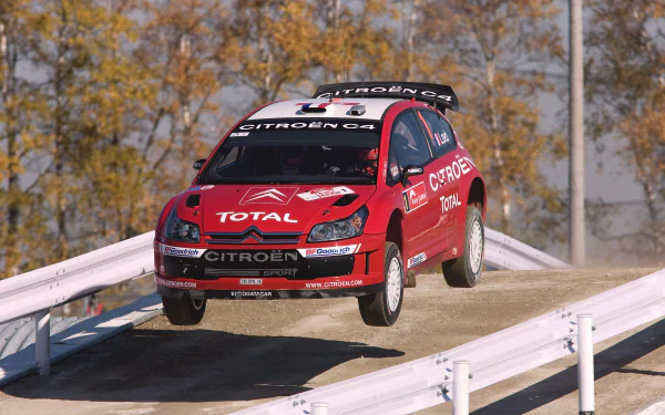 HD desktop wallpaper featuring a red Citroën rally car racing mid-air on a dirt track, showcasing rallying and motorsport excitement.