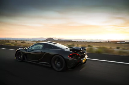 HD PC desktop wallpaper featuring a sleek black McLaren P1 speeding along an open road at sunset.