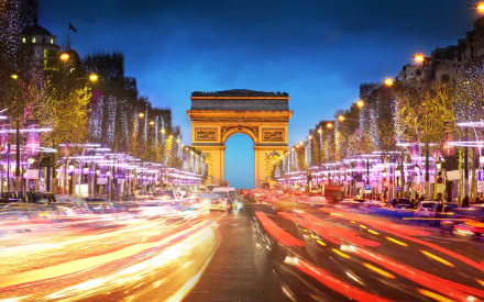 Time-lapse view of the colorful Champs-Élysées at night with light trails leading to the illuminated Arc de Triomphe in Paris, France.