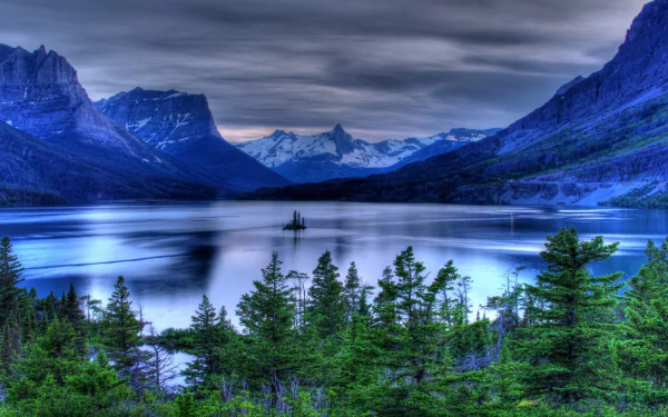 HD desktop wallpaper showcasing the serene beauty of nature at Saint Mary Lake, with calm waters, lush greenery, and snow-capped mountains under a dramatic sky.