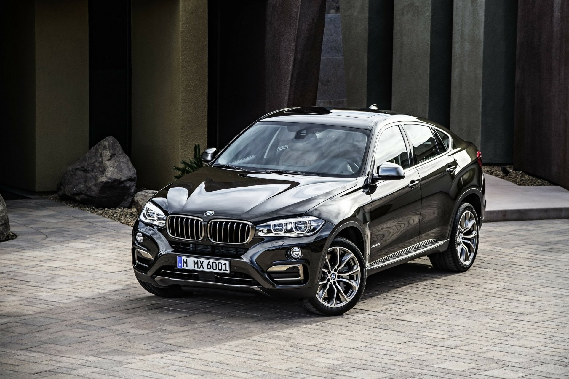 HD PC desktop wallpaper featuring a sleek black BMW X6 parked on a stone driveway with modern architectural elements in the background.