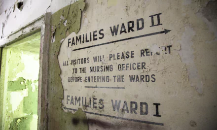 5K Ultra HD PC wallpaper: HDR photo of an urban ruin in Germany — rusted, peeling hospital wall stenciled 'Families Ward II', green-lit doorway in a decayed man-made interior.