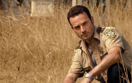 Rick Grimes, portrayed by Andrew Lincoln, kneels in a field of dry grass, capturing the post-apocalyptic essence of *The Walking Dead* in this HD desktop wallpaper.