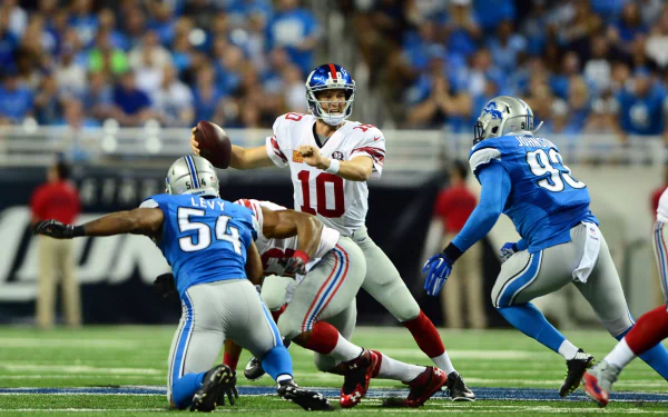 HD PC desktop wallpaper showing Detroit Lions defenders closing on a Giants quarterback dropping back to pass, action shot on the field with a blurred stadium crowd in the background.