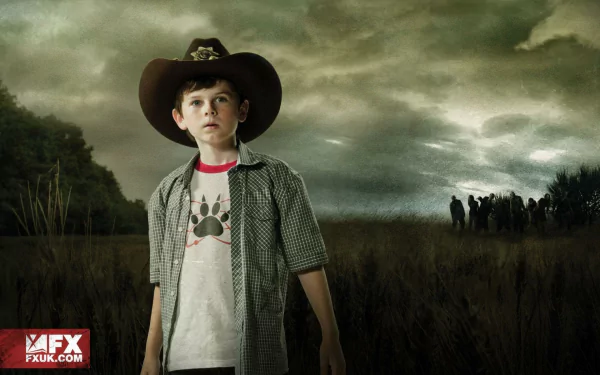 Chandler Riggs as Carl Grimes stands confidently in a desolate landscape, wearing a cowboy hat against a dramatic sky, evoking the intense atmosphere of *The Walking Dead*.
