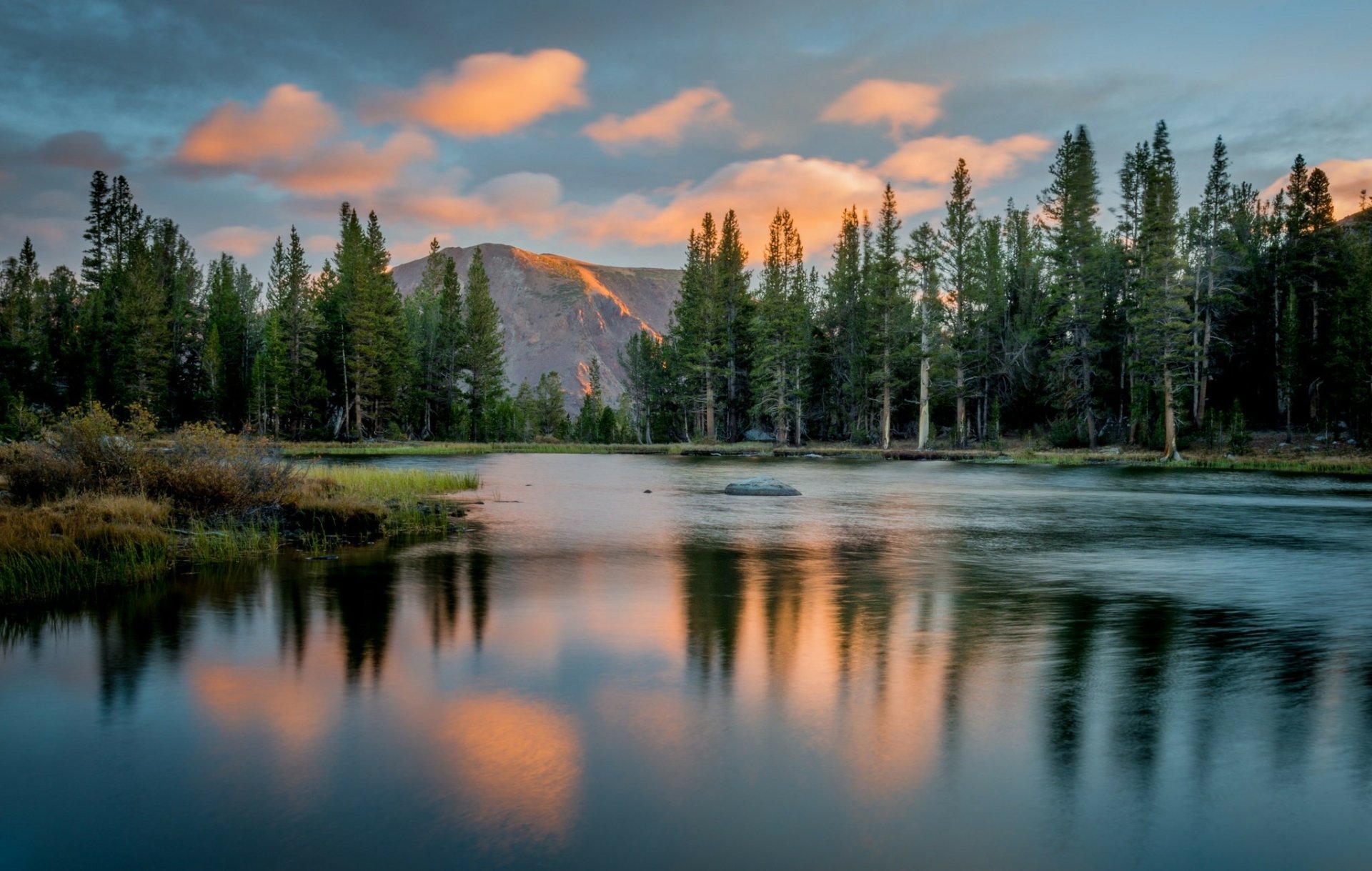 HD desktop wallpaper featuring a serene mountain landscape with a forest and calm lake reflecting a colorful sunset sky.