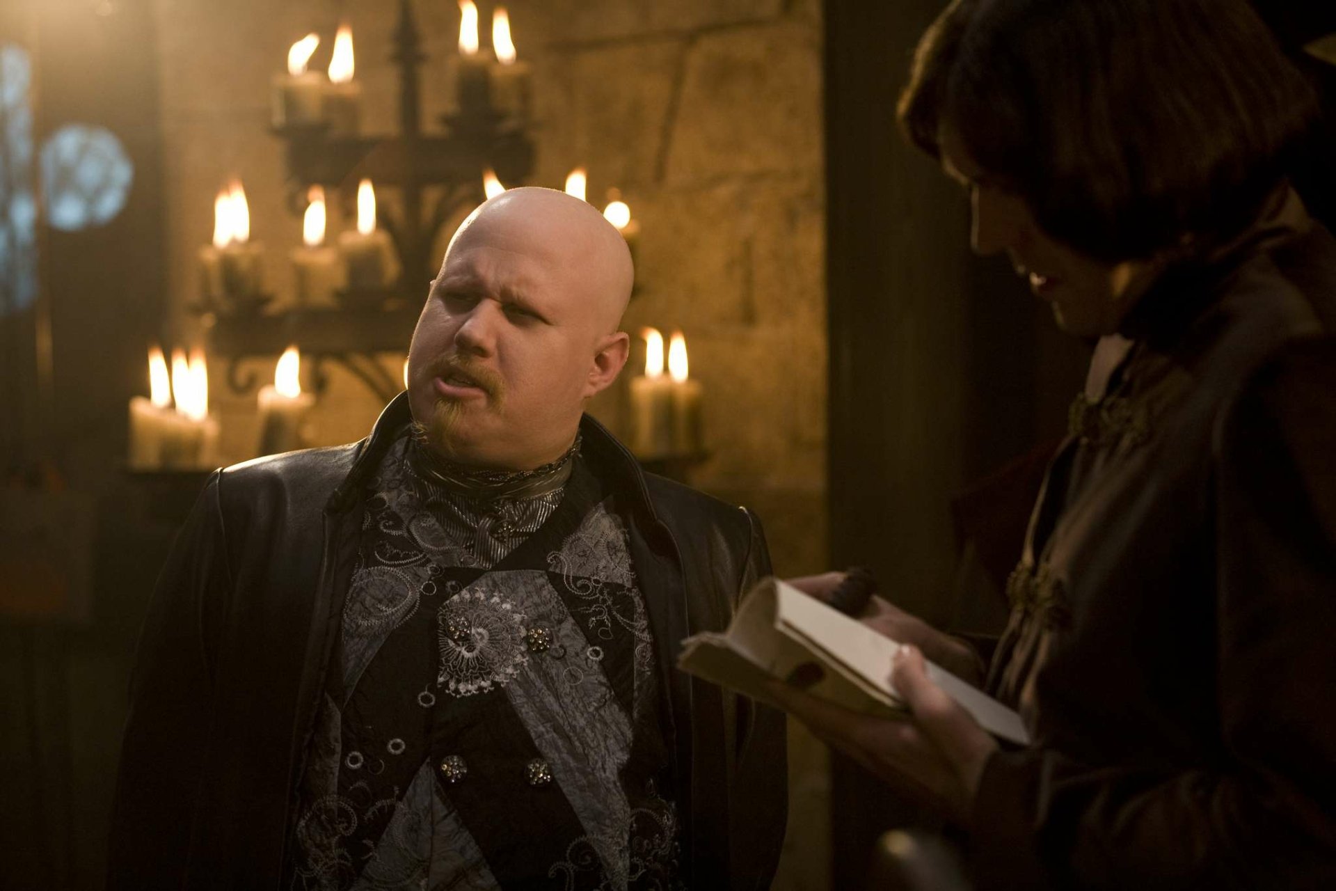 Kröd Mändoon and the Flaming Sword of Fire TV show HD desktop wallpaper: bald man in ornate dark robes in a candlelit medieval chamber speaking to a robed scribe.