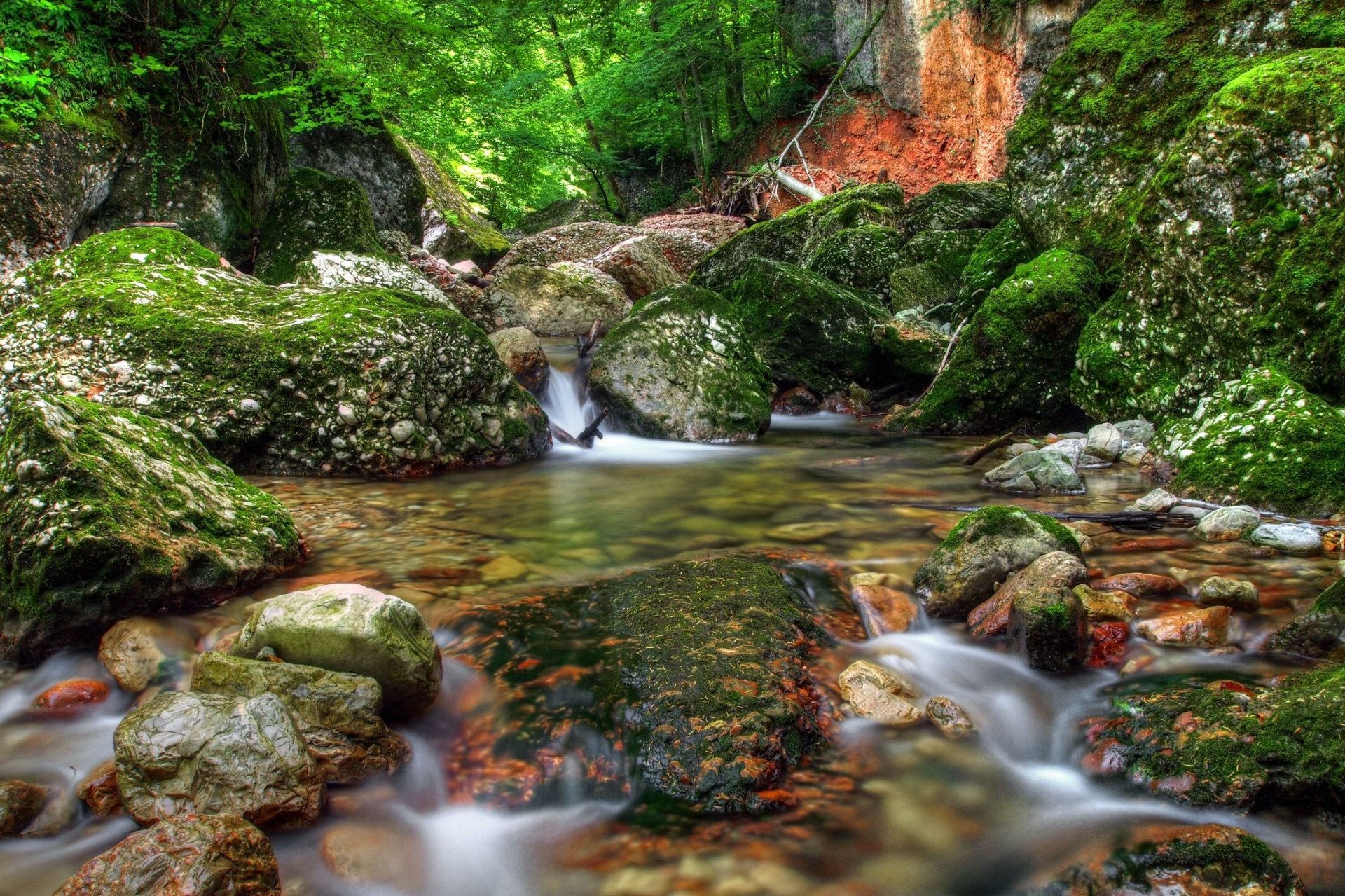 A serene nature scene with moss-covered rocks and a gently flowing stream captured with motion blur, presented as an HD PC desktop wallpaper and background.