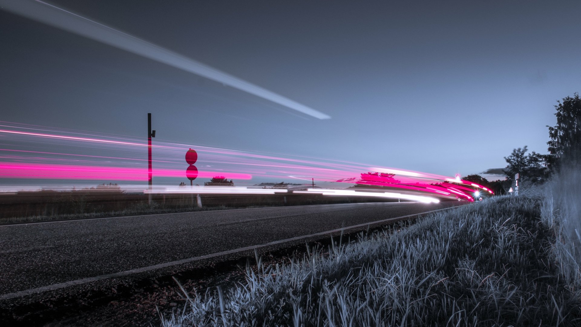 4K Ultra HD PC desktop wallpaper background of a man-made road at dusk, long-exposure pink and white light trails sweeping past a roadside sign and frost-tipped grass under a clear sky.