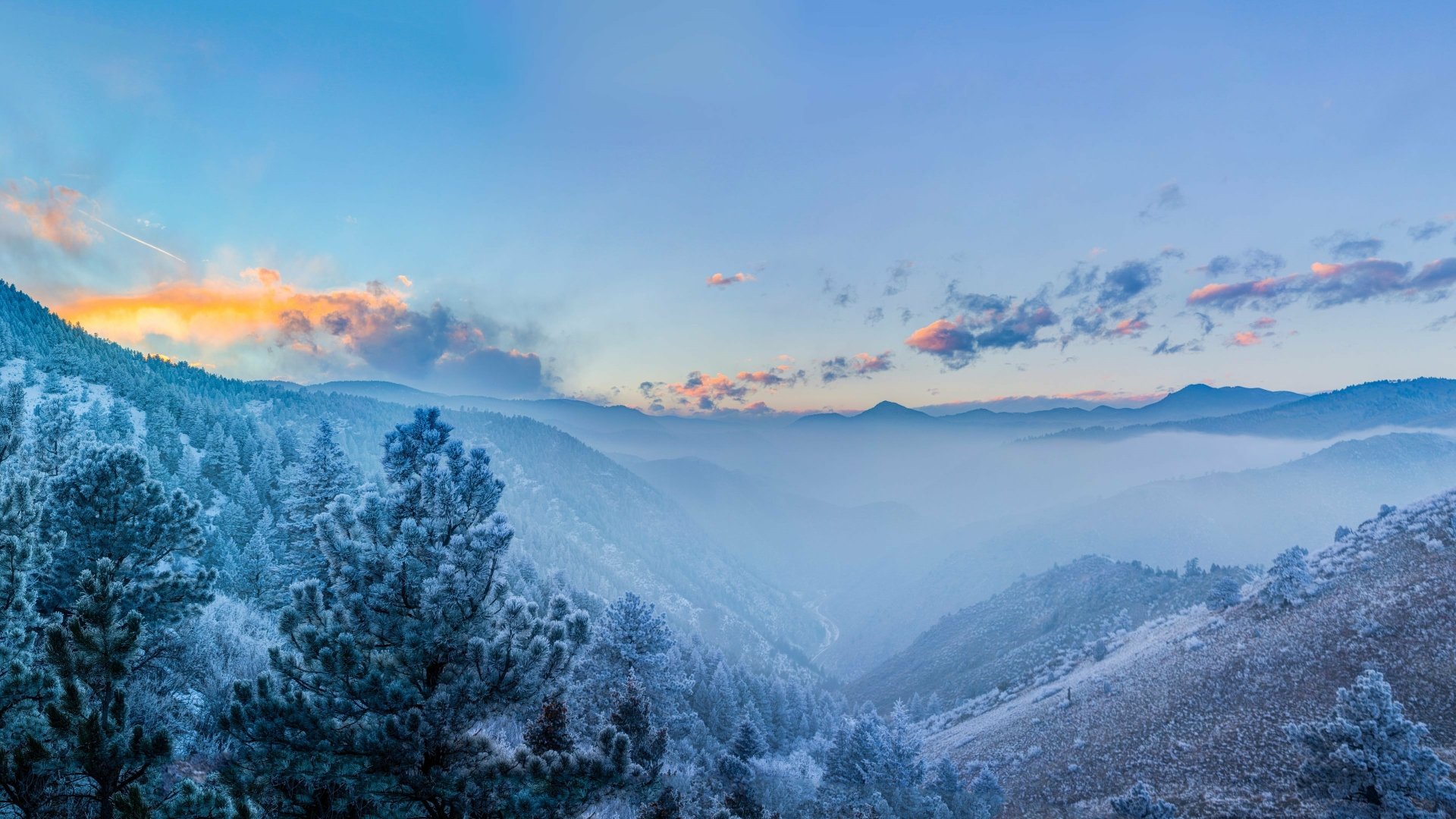 4K Ultra HD winter landscape wallpaper featuring snow-covered trees and misty mountains under a colorful dawn sky.