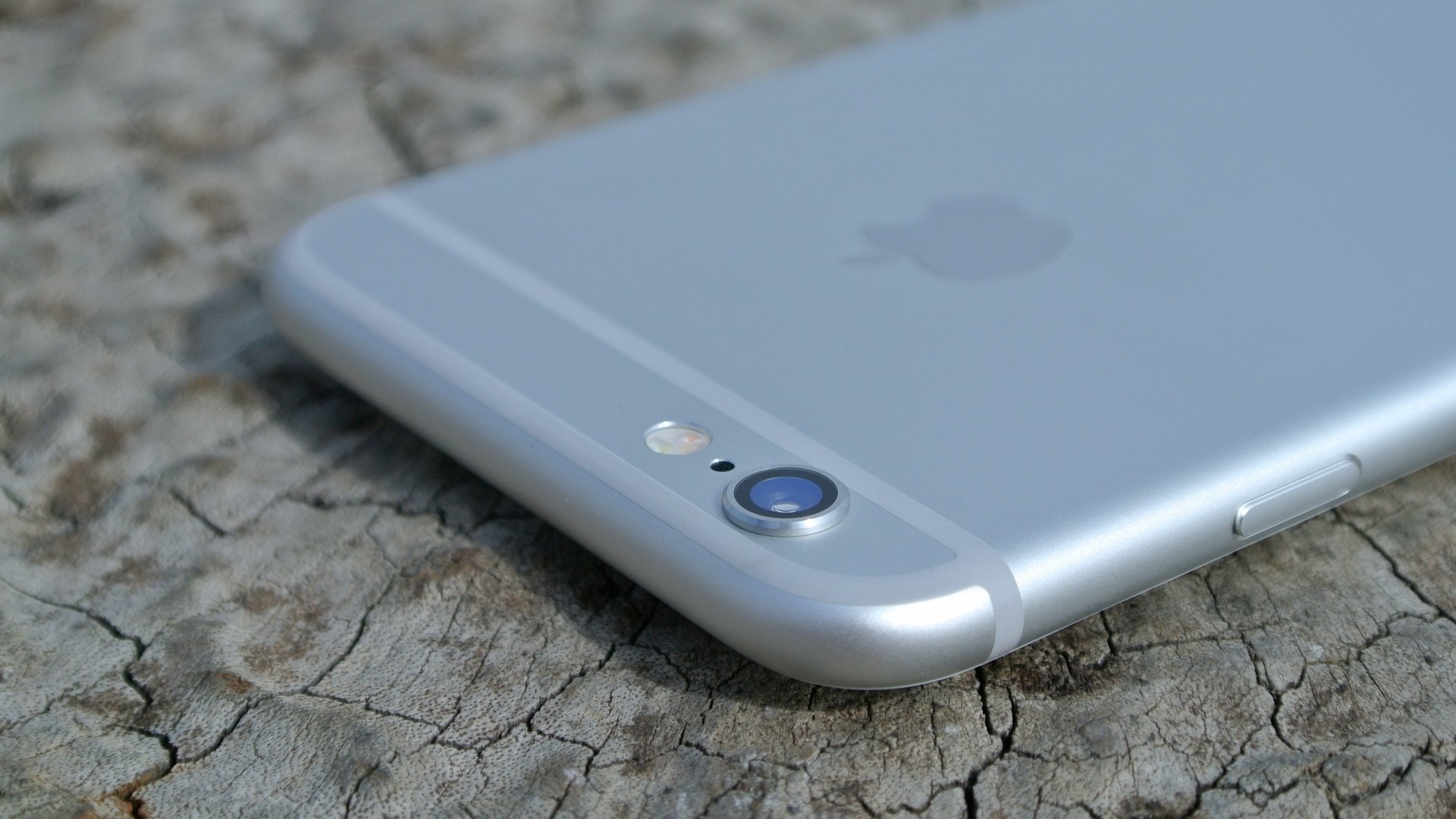 Close-up of a silver iPhone camera and Apple logo on cracked stone, styled as a 4K Ultra HD PC desktop wallpaper background highlighting technology.