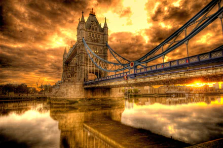 HD wallpaper of Tower Bridge in London, England, illuminated under a vivid sunset with dramatic clouds and reflections in the water.