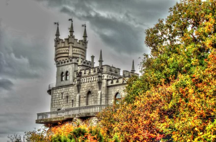 HD wallpaper of Russia's iconic Swallow's Nest castle perched above colorful autumn foliage in Yalta, showcasing intricate man-made architecture against a cloudy sky.