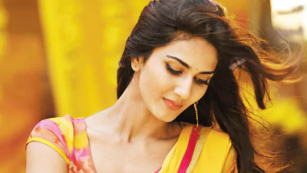 HD desktop wallpaper featuring Bollywood celebrity Vaani Kapoor with a serene expression and flowing hair against a vibrant yellow background.