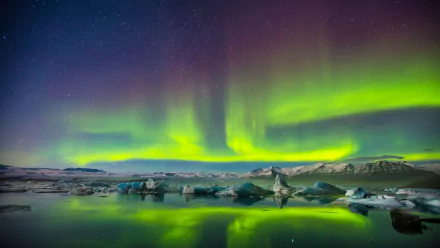 HD wallpaper featuring the aurora borealis over a snowy landscape at night, reflecting in a serene water body.