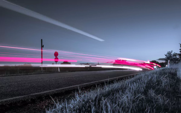 4K Ultra HD PC desktop wallpaper background of a man-made road at dusk, long-exposure pink and white light trails sweeping past a roadside sign and frost-tipped grass under a clear sky.