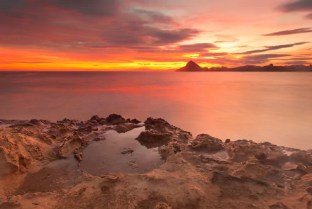 HD desktop wallpaper showcasing a vibrant sunset over the sea in Spain, with dramatic clouds and rocky shore in the foreground highlighting nature's beauty.