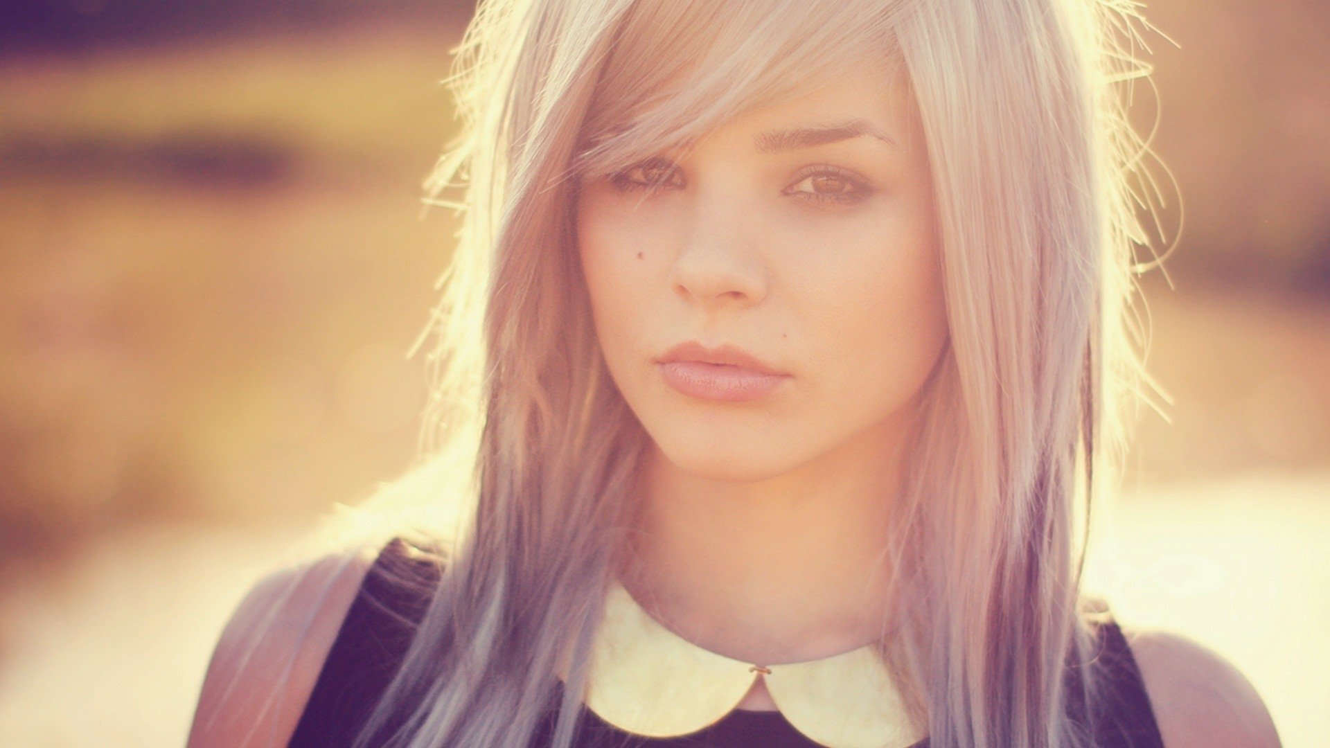 HD wallpaper featuring a woman with long, light hair and a serene expression, set against a softly blurred, sunlit background.